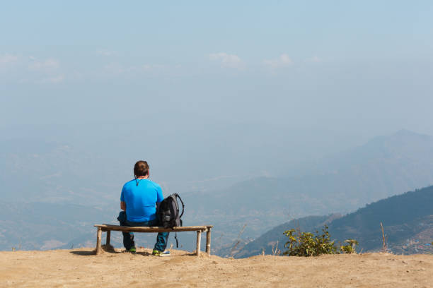A man with a backpack sits on a bench looking to the horizon. Kathmandu. Nagarkot. View point on the mountains of Nepal. Landmark. A man with a backpack sits on a bench looking to the horizon. Kathmandu. Nagarkot. View point on the mountains of Nepal. Landmark. nagarkot photos stock pictures, royalty-free photos & images