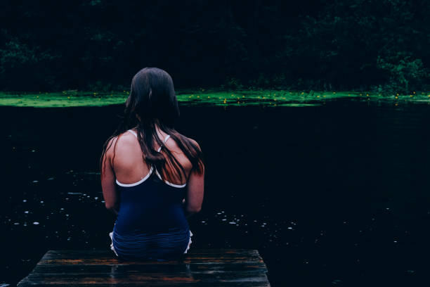 Girl sitting on pier looking back. Child swimming in lake. Spending time actively outdoors. Childhood memories. Having time outside in summer. Beautiful scenic background, backdrop