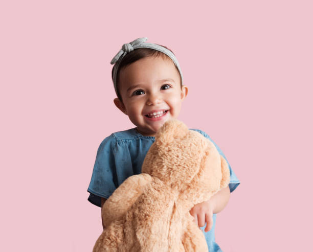 A very happy little girl with a big smile holding a teddy bear in front of her as she faces the camera.