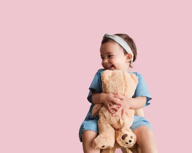 A little girl hugging her teddy bear with both hands and smiling as she looks away from the camera.