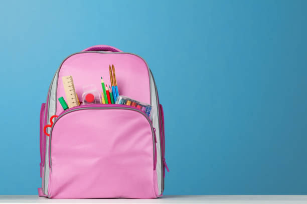 mochila rosa con artículos de oficina sobre la mesa sobre un fondo azul. regreso a la escuela. - open book teaching table fotografías e imágenes de stock