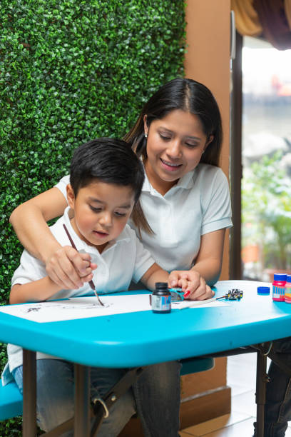 mamma aiuta il suo figlio di 4 anni dipingere con un pennello - home interior young adult professional occupation vertical foto e immagini stock