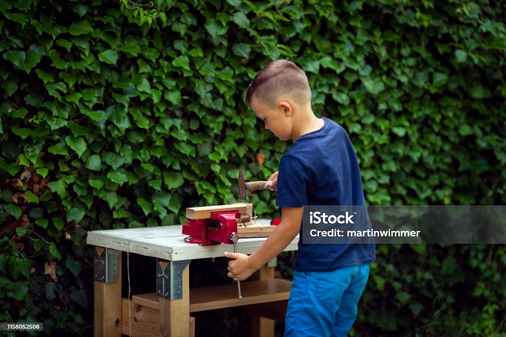 little working boy in a garden at a workbench Germany, 7 year old little boy working working at a workbench in the garden 6-7 Years Stock Photo