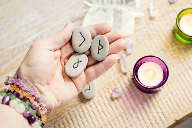 Photo of Holding rune stones in hand. Candles burning on light wooden background.