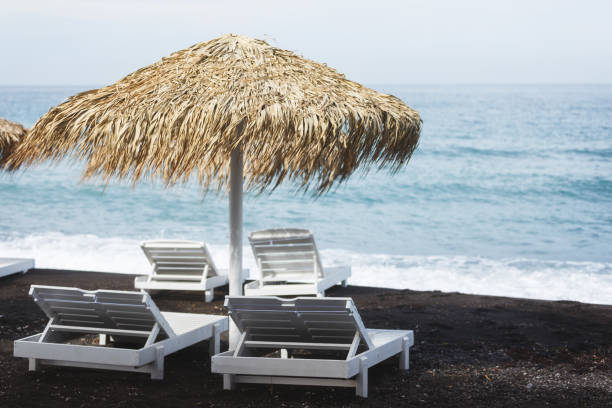 strandstrohschirm und strandbetten mit meerblick, insel santorin, griechenland - black sand beach santorini greece stock-fotos und bilder