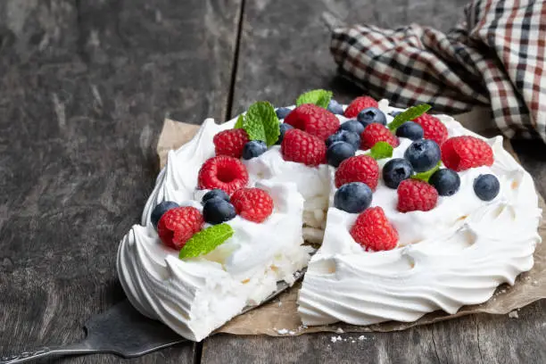 Pavlova  meringue nest with berries and mint leaves on wooden table