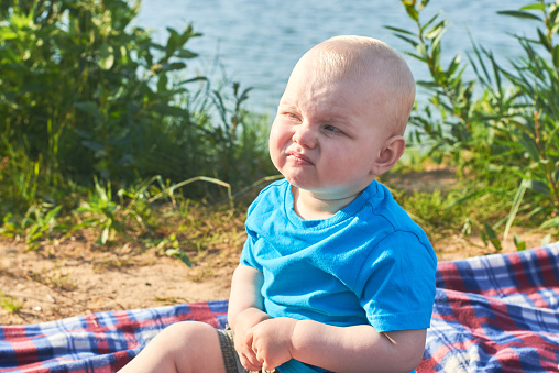 Portrait of a funny little boy who grimaces, on the river bank on a summer day