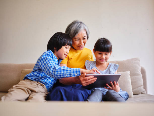 Grandmother Reading to Children in a Home in Taiwan A Taiwanese grandmother reads from an electronic tablet to her grandchildren in a home in Taipei. asian nanny stock pictures, royalty-free photos & images