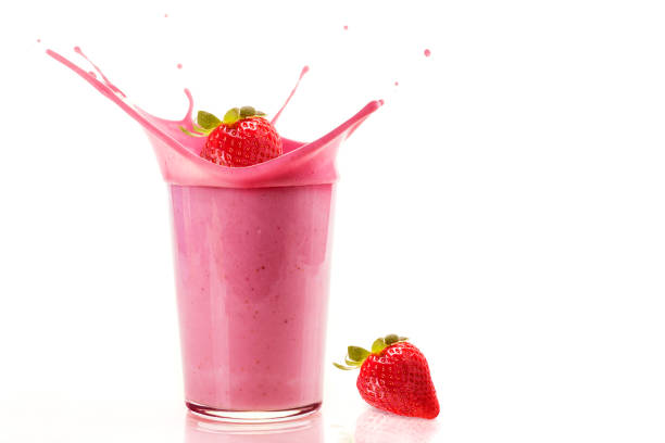 Delicious strawberries falling into a glass of strawberry milkshake on white background stock photo