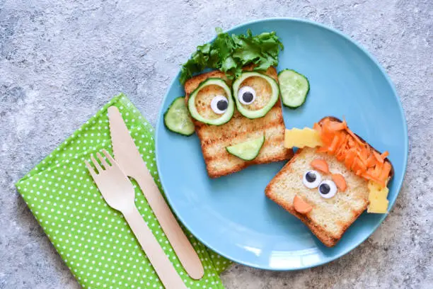 Photo of Funny faces - lunch for the child. Sandwich with vegetables. View from above.
