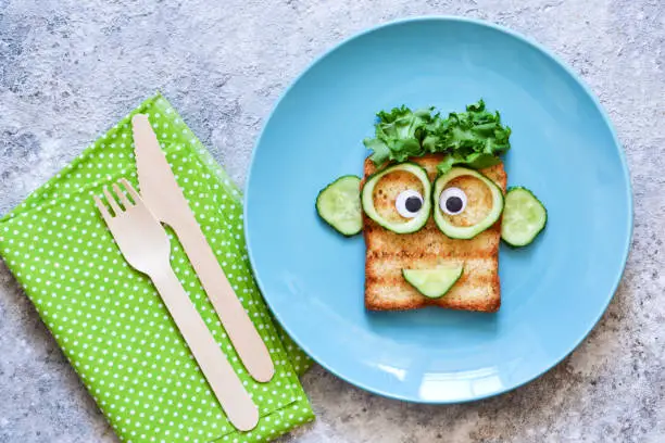 Photo of Funny faces - lunch for the child. Sandwich with vegetables. View from above.