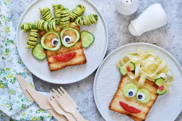 Photo of Lunch for children. Pasta with sandwiches and vegetables. Cheerful face.