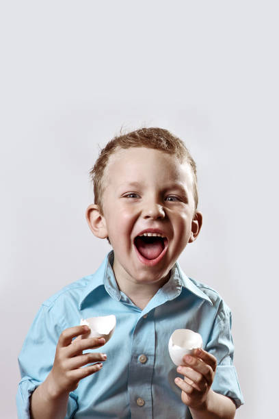 istock boy in a light shirt holding a shell from the egg and smiling on a light background 1158071575