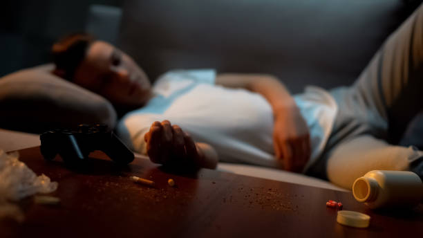 adolescente maschio che dorme in una stanza disordinata, sigaretta e pillole sul tavolo, dipendenza da gioco - narcotic teenager marijuana drug abuse foto e immagini stock