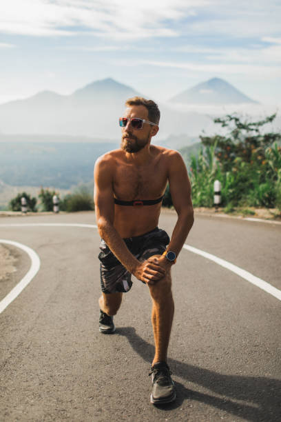 istock Runner doing lunges and warming-up before running on the road. Summer weather, topless body and sunglasses. 1158072997