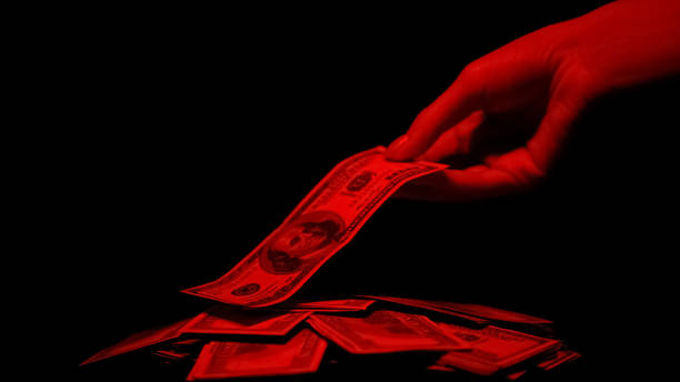 рука принимая доллар из кучи освещены красным светом, кровавые деньги преступления вознаграждение - money laundering стоковые фото и изображения