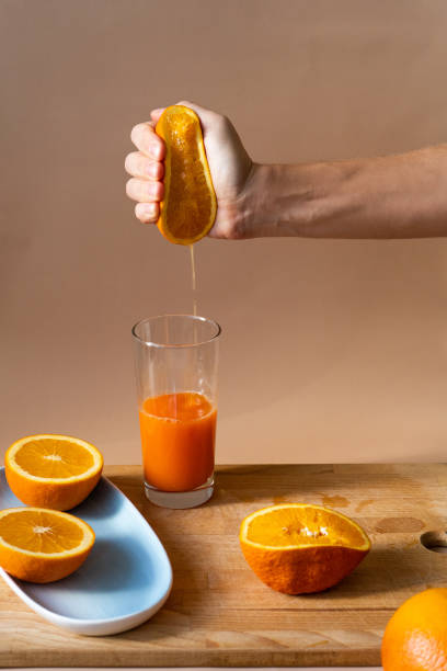 female hand squeezes fresh cold orange into the glass. sliced citrus on a wooden board and a blue plate. orange juice for breakfast, vitamins for health. - freshly squeezed orange juice imagens e fotografias de stock