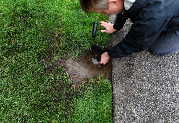 Sprinkler system being repaired by mature man with irrigation parts laying on ground stock photo