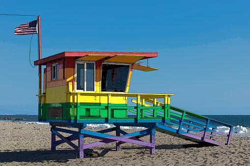 The pride colored lifeguard hut tower in Venice Beach near the boardwalk in honor of Bill Rosendahl flying the American flag