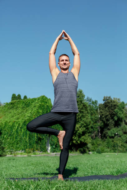 istock Healthy Lifestyle. Man practicing yoga on mat outdoors in one-legged prayer pose hands up concentrated 1158086570
