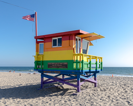 The pride colored lifeguard hut tower in Venice Beach near the boardwalk in honor of Bill Rosendahl first openly gay man elected to the Los Angeles City Council, flying the American flag
