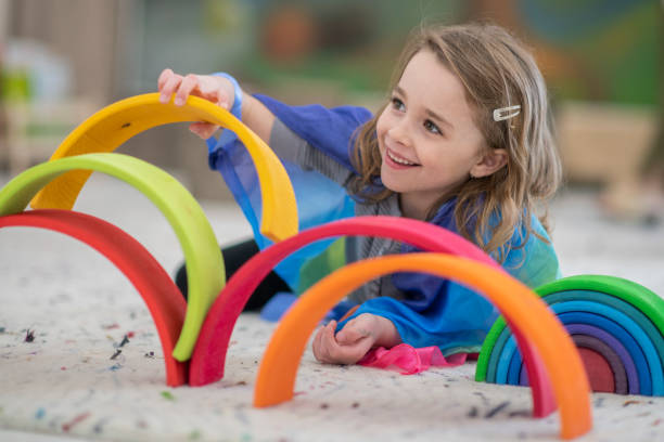 Cute elementary girl building a rainbow structure A girl places colourful rings on top of each other while smiling off to the side. She is lying on the carpet of a classroom. She is dressed casually. montessori education stock pictures, royalty-free photos & images