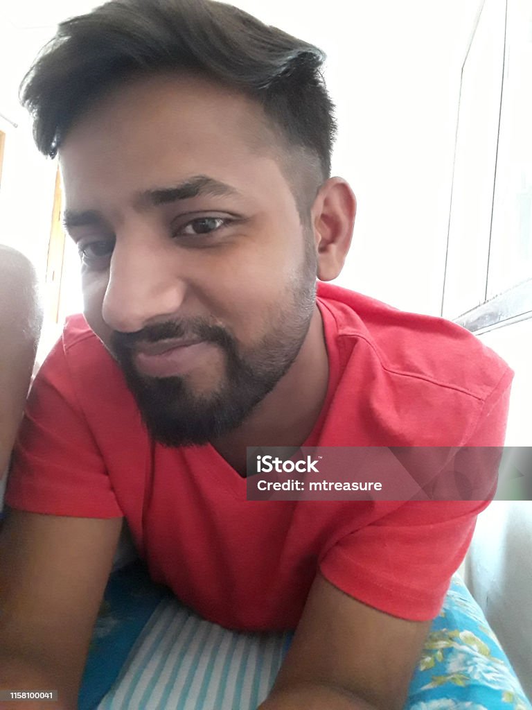 Image Of Young Happy Smiling Handsome Indian Man In Early 20s Lying On Bed  Wearing Red Vneck Tshirt Trendy Hairstyle Short Hair At Side And Neatly  Trimmed Beard Good Looking Hindu Guy