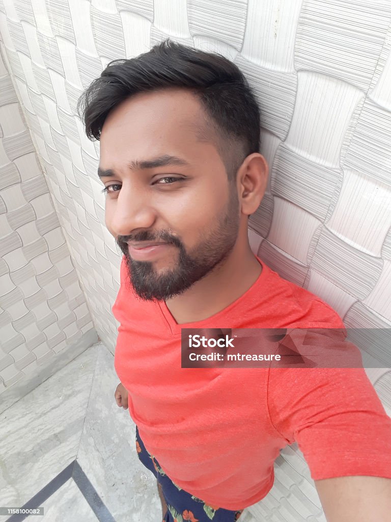 Image Of Young Happy Smiling Handsome Indian Man In Early 20s Wearing Red  Vneck Tshirt Taking Self Portrait Selfie Photo On Mobile Phone Camera  Standing By Textured Wallpaper With Checks Trendy Hairstyle