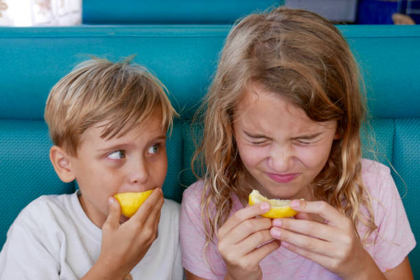 dzieci gryzące w cytryny i robiące twarze - lemon sour taste biting eating zdjęcia i obrazy z banku zdjęć