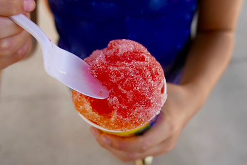 Close up of a colorful snow cone being eaten by a girl with a plastic spoon