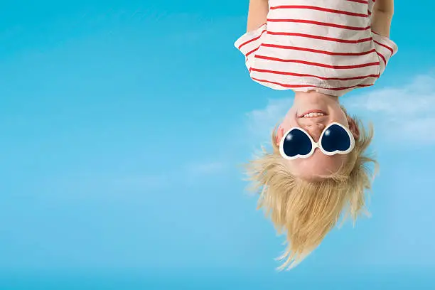 Young child wearing heart shaped sunglasses, carefree having fun hanging upside down.