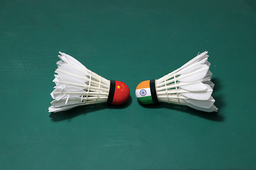 Two used shuttlecocks on green floor of Badminton court with both head each other. One head painted with China flag and one head painted with the India flag, concept of badminton competition.