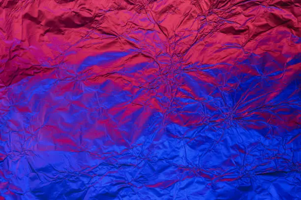Blue red deformed background made of neon lights foil. Trendy duotone texture.