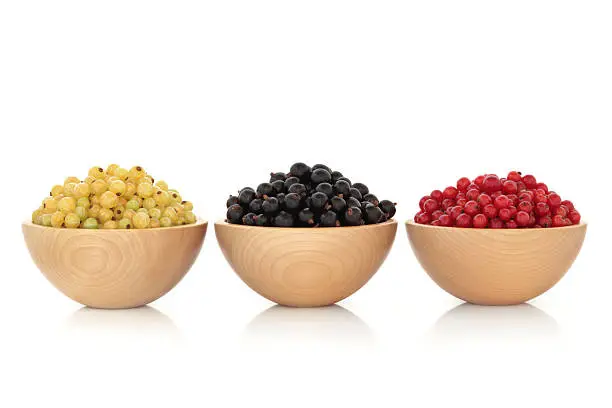Whitecurrant, blackcurrant and redcurrant fruit in beech wood bowls, isolated over white background.