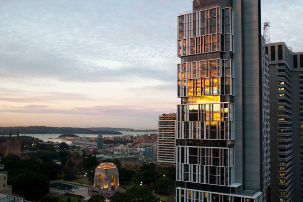 coucher du soleil se reflétant dans le verre de l'immeuble d'appartements de gratte-ciel avec le mémorial d'anzac dans hyde park et port à l'arrière-plan - tower building photos et images de collection