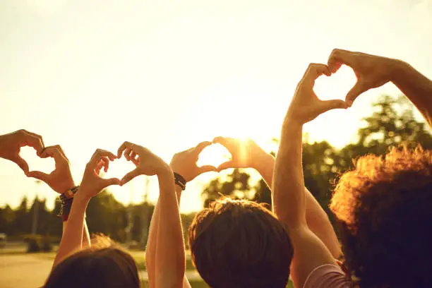 Photo of Hands of group friends in the shape of a heart against the sunset.