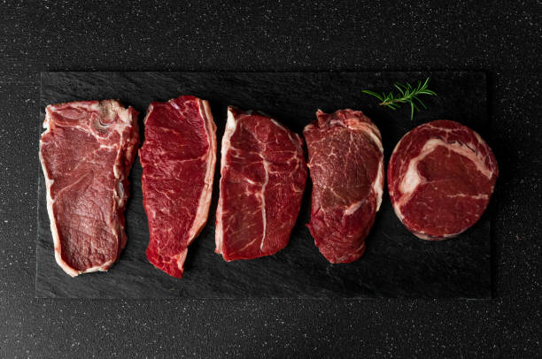 Selection of raw beef meat food steaks against black stone background. New york striploin steak, top blade, rib eye, and other cuts of meat. stock photo
