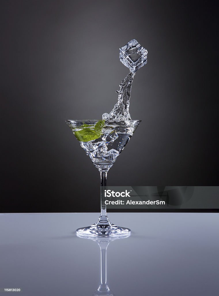 Iice cube jumps out from a glass of martini. The ice cube jumps out from a glass with martini and mint.. Alcohol - Drink Stock Photo