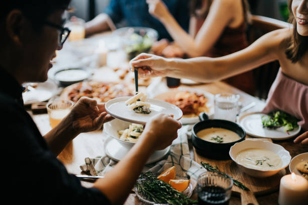 junge asiatische frau serviert pasta zu freunden während der party, sie haben spaß, plaudern und genießen essen und getränke - asian cuisine lunch dinner food stock-fotos und bilder