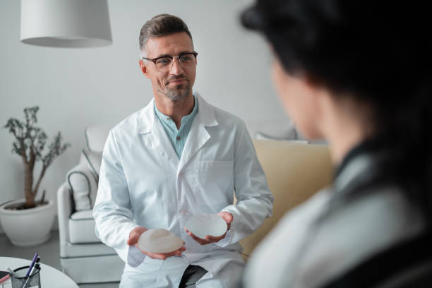 istock Pleasant plastic surgeon wearing glasses showing breast implants 1158131510