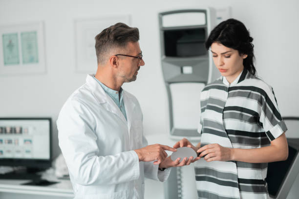 istock Plastic surgeon wearing glasses showing client implants for breast 1158131513