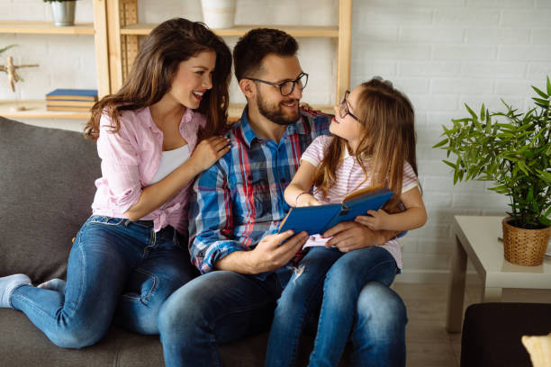 istock Young girl reading book while sitting on sofa with her parents 1158134718
