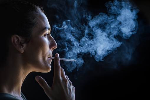 Vista de perfil de una hermosa mujer fumando en la oscuridad. photo