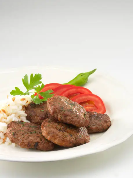 Meatball or turkish köfte with lettuce salad and green pepper and tomatoes in plate.