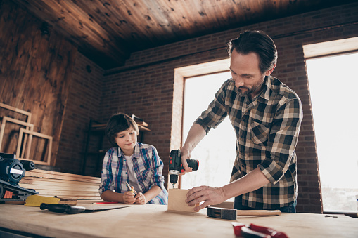 Portrait of charming nice pretty focused son father hold hand have, equipment craftsmen apprentice diy teacher workplace home hobby wear checkered shirt beard studio industrial interior