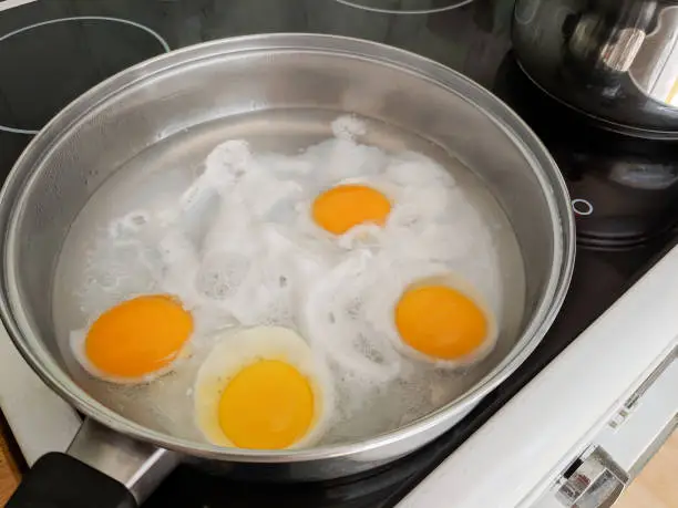 Poaching fresh eggs in a pan of water in an authentic kitchen environment. Four eggs part way through being cooked.
