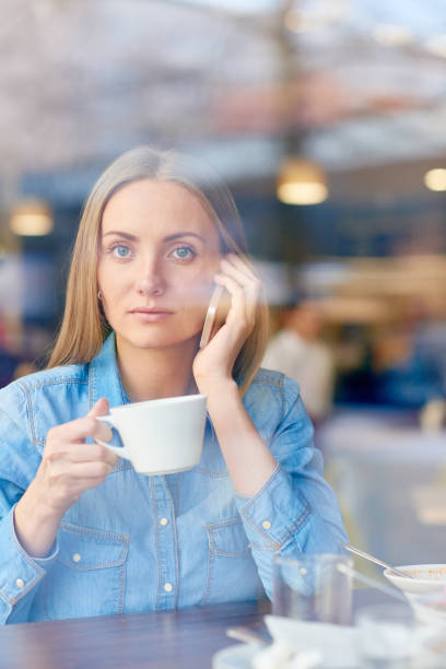 istock Woman with beverage answering phone and looking at camera 1158156827