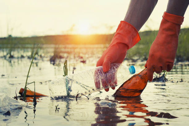 woman hand picking up garbage plastic for cleaning at river with sunset