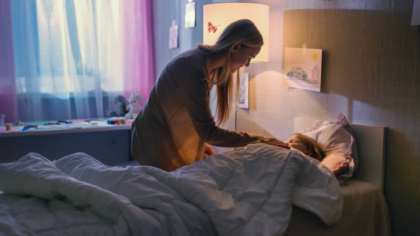 la giovane madre amorevole si infila nella sua graziosa figlia piccola e dice "buona notte". - bedtime foto e immagini stock