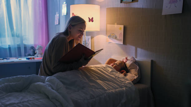 jeune mère aimante lit des histoires de coucher à sa petite belle fille qui va dormir dans son lit. - bedtime photos et images de collection